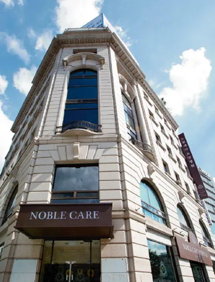노블케어요양병원 1관 외관. 석조 건물 모서리에 NOBLE CARE 차양이 걸려 있다