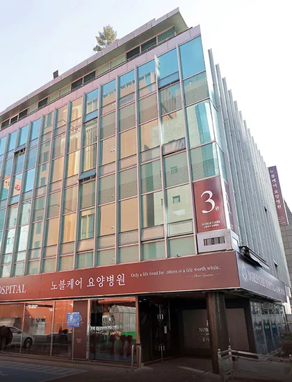 노블케어요양병원 3관 외관. 붉은 띠 간판과 3관 세로 배너가 보인다