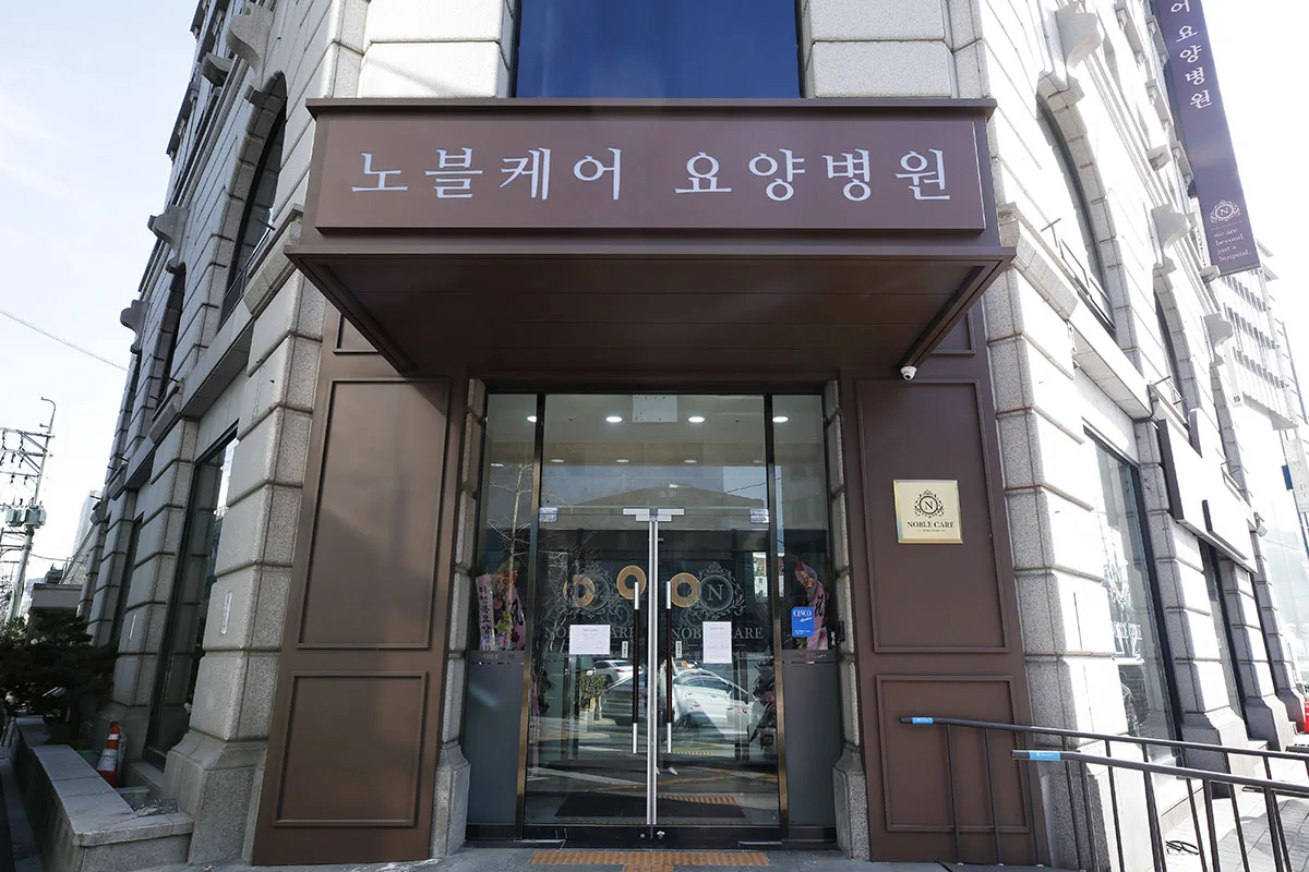 노블케어요양병원 1관 정문. 갈색 프레임 유리문 위에 한글 간판이 있다