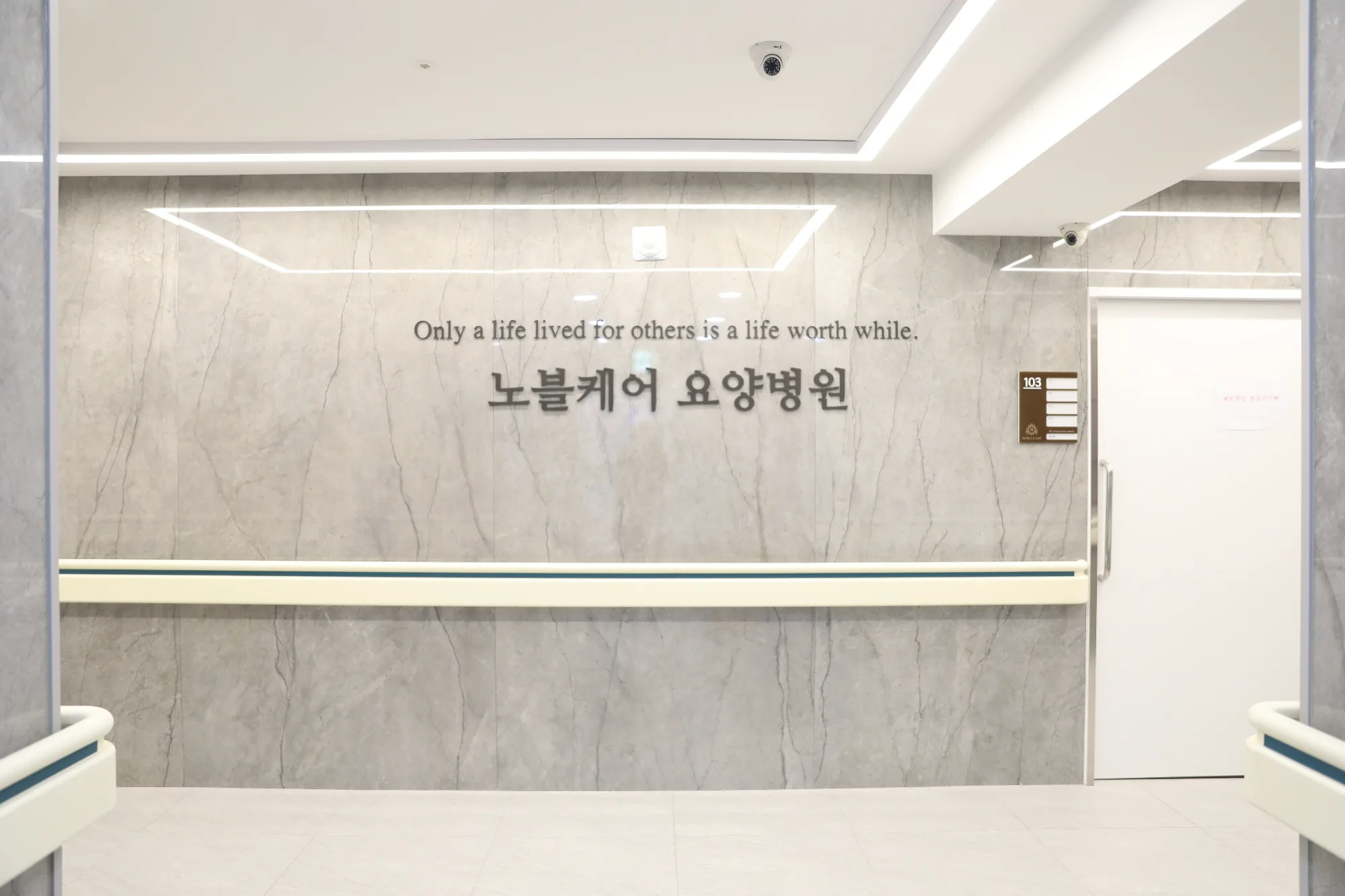 로비 대리석 벽면에 새겨진 노블케어 요양병원 이름과 Only a life lived for others is a life worth while 문구