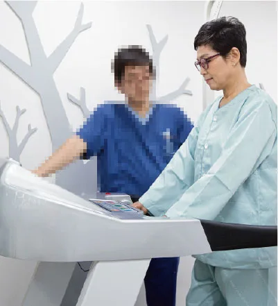 환자가 보행 훈련 기구를 잡고 걷는 연습을 하고 치료사가 옆에서 돕고 있다