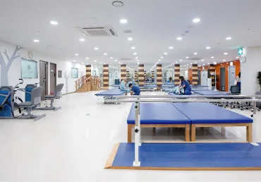 물리치료실 전경. 파란 치료 베드가 줄지어 있고 나무 계단 훈련 기구가 있다