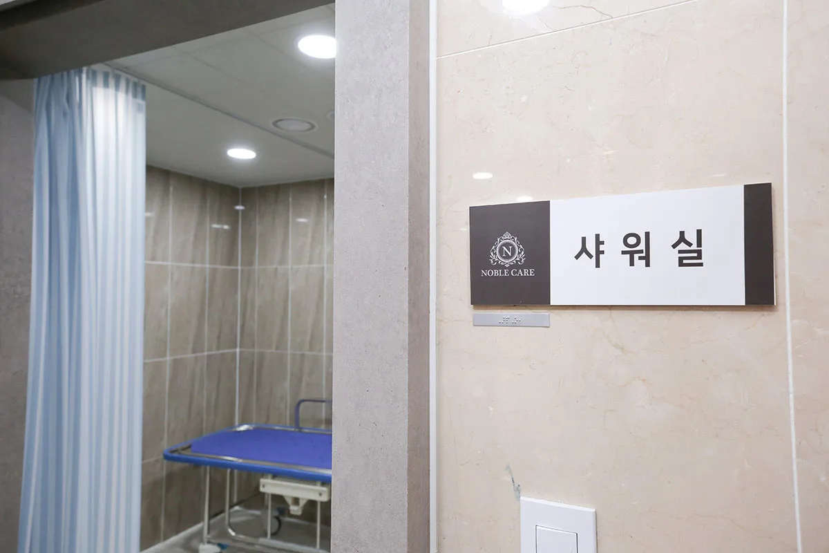샤워실 입구. 노블케어 엠블럼이 있는 샤워실 명패와 샤워 의자